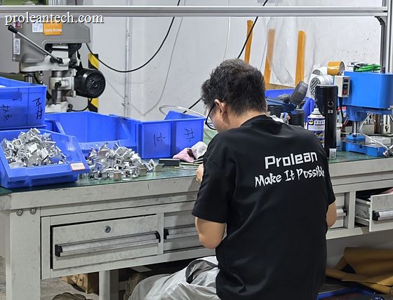 An operator in a Proleantech work shirt sorting machined parts into blue bins at a bench