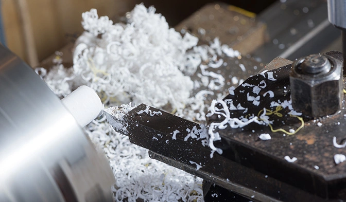 A single-point turning tool removing material from a Delrin rod