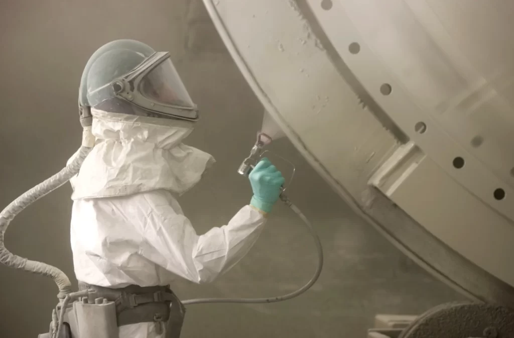 Worker in PPE airless spraying large industrial tank 