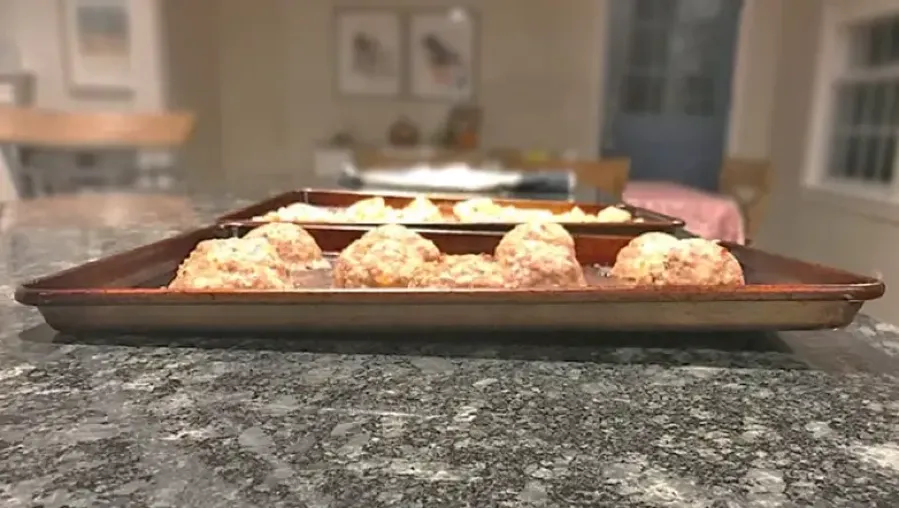 Warped stainless steel baking pan with uneven base holding biscuits
