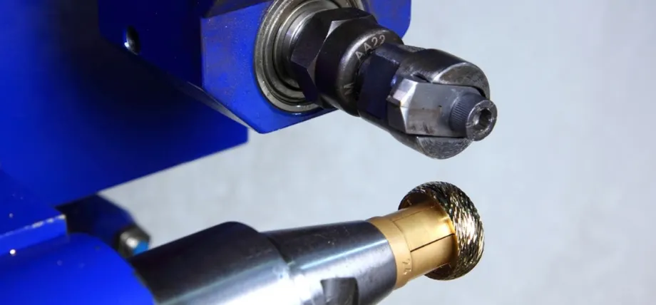 Blue CNC machine applying detailed textured patterns to a gold cylindrical jewelry component.