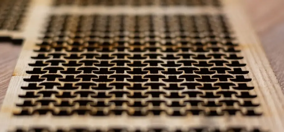 A CO2 laser cutting head emitting a red beam as it engraves or cuts a transparent acrylic sheet on a honeycomb bed inside a laser cutting machine.