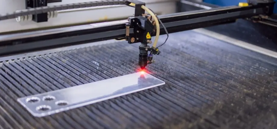 Close-up of acrylic sheet with precision-cut holes and a laser beam cutting on edge of the acrylic sheet.