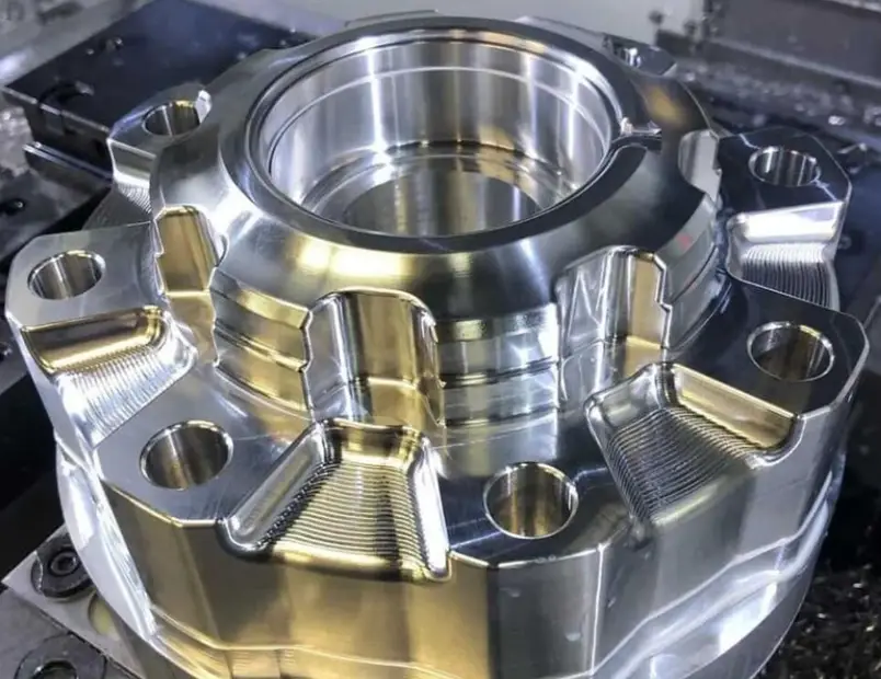An intricate shiny cylindrical part with mounting holes showing a CNC machined aerospace part