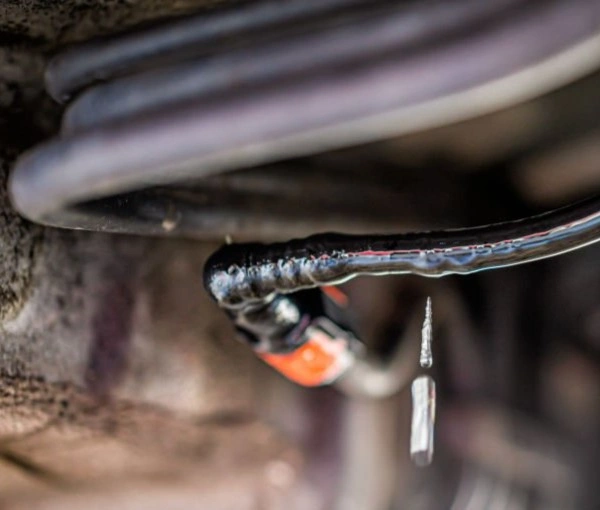 A closeup image of liquid droplets falling from the surface of a line underneath a car with an orange connector suggesting a high-pressure system
