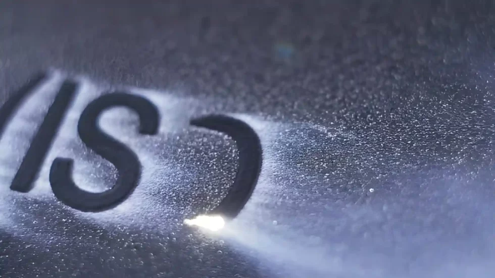 A laser engraver etches text codes onto a metal surface for identification and traceability.