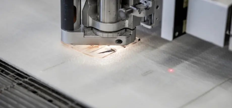 Precision laser head with red alignment beam cutting intricate patterns into white textile material on a honeycomb bed during laser cutting materials process.