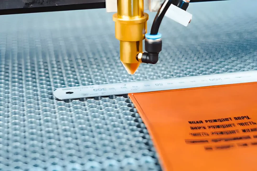 The image shows a CO₂ laser cutting machine cutting the corners of a plastic sheet, with a scale placed for reference.