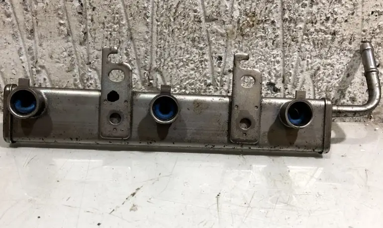 An image of a metal fuel injector rail showing ports, seals, and mounting brackets 