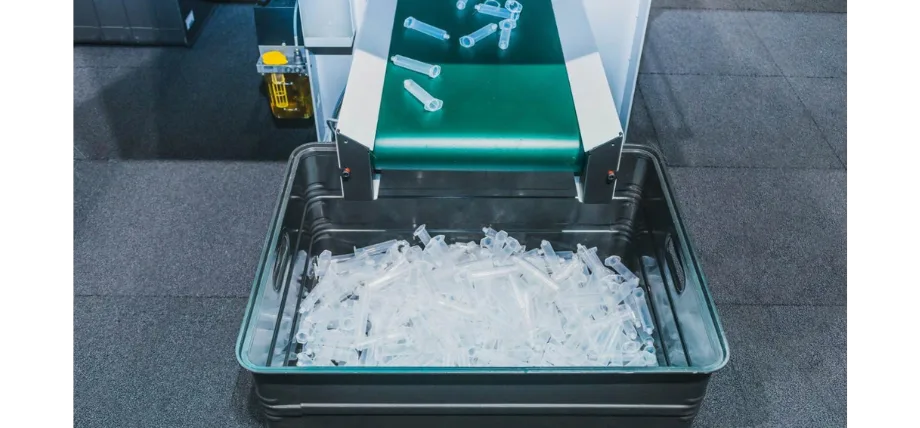 green conveyor belt sliding white plastic parts in a bucket