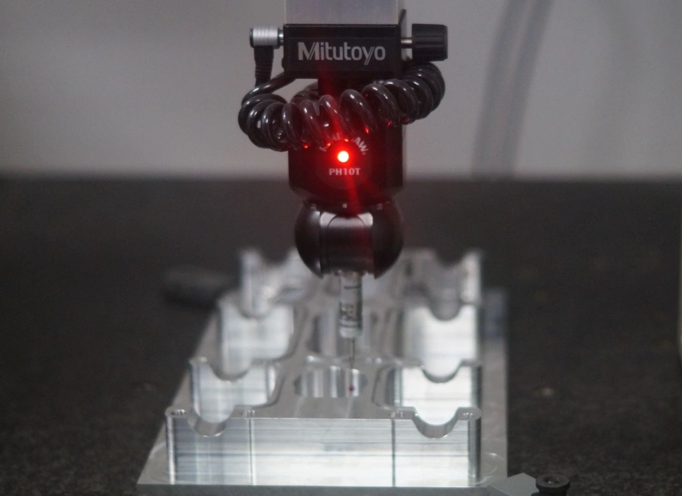 An image of a sophisticated compact machine called a Coordinate Measuring Machine (CMM) on a metal plate with machined contours 