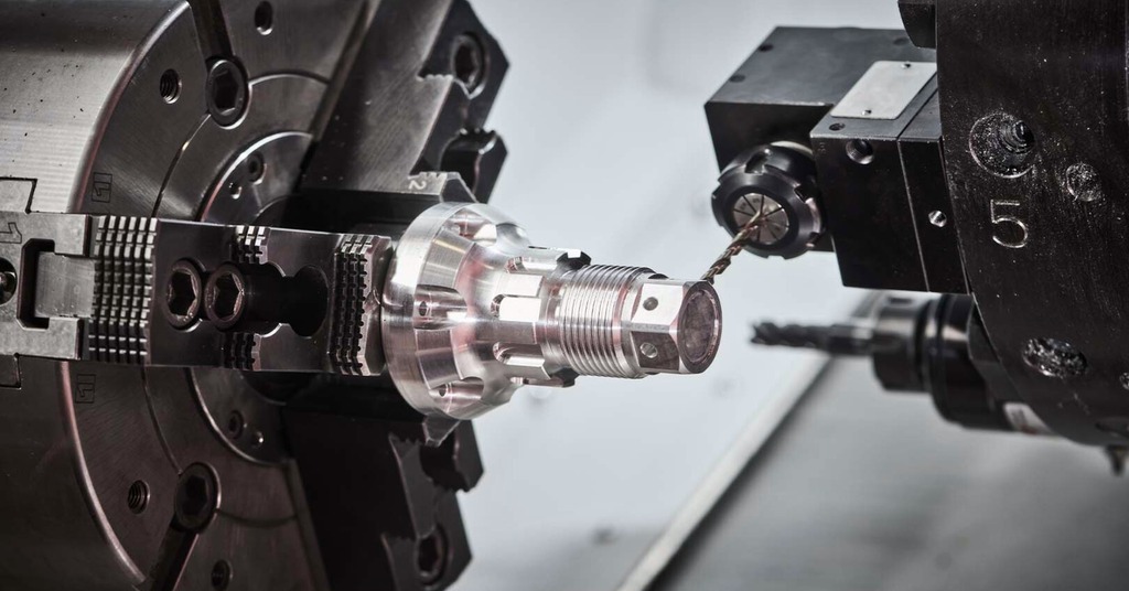 CNC turning and drilling operation on a precision metal component, held in a lathe chuck, with a cutting tool machining fine features and holes on the cylindrical part.