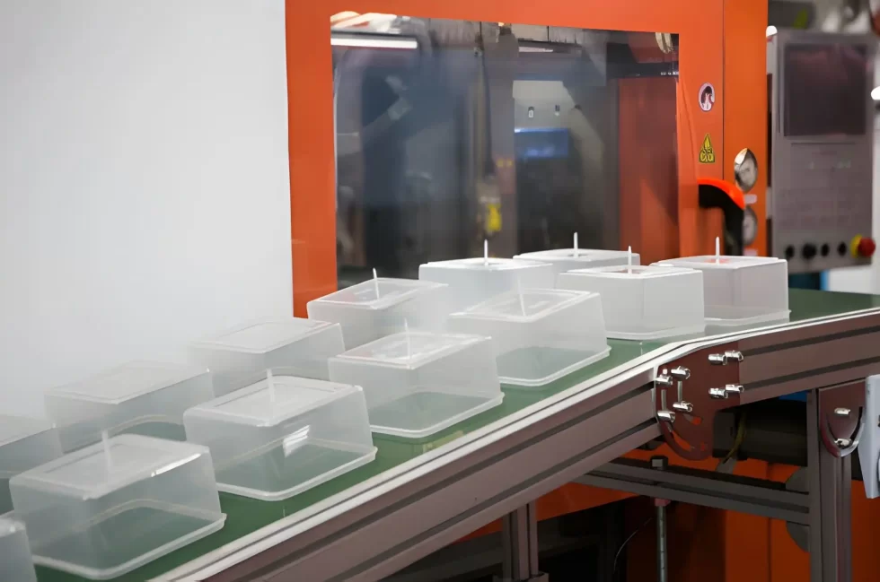Multiple identical transparent square plastic enclosures on a conveyor.